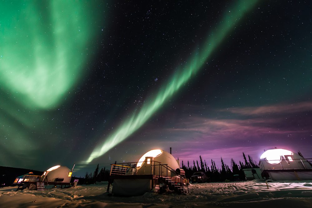 Aurora Borealis lighting up the night sky over a snow-covered cabin in Alaska.