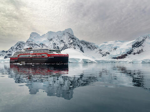 A ship navigating through icy waters near the Antarctic Peninsula, surrounded by penguins.